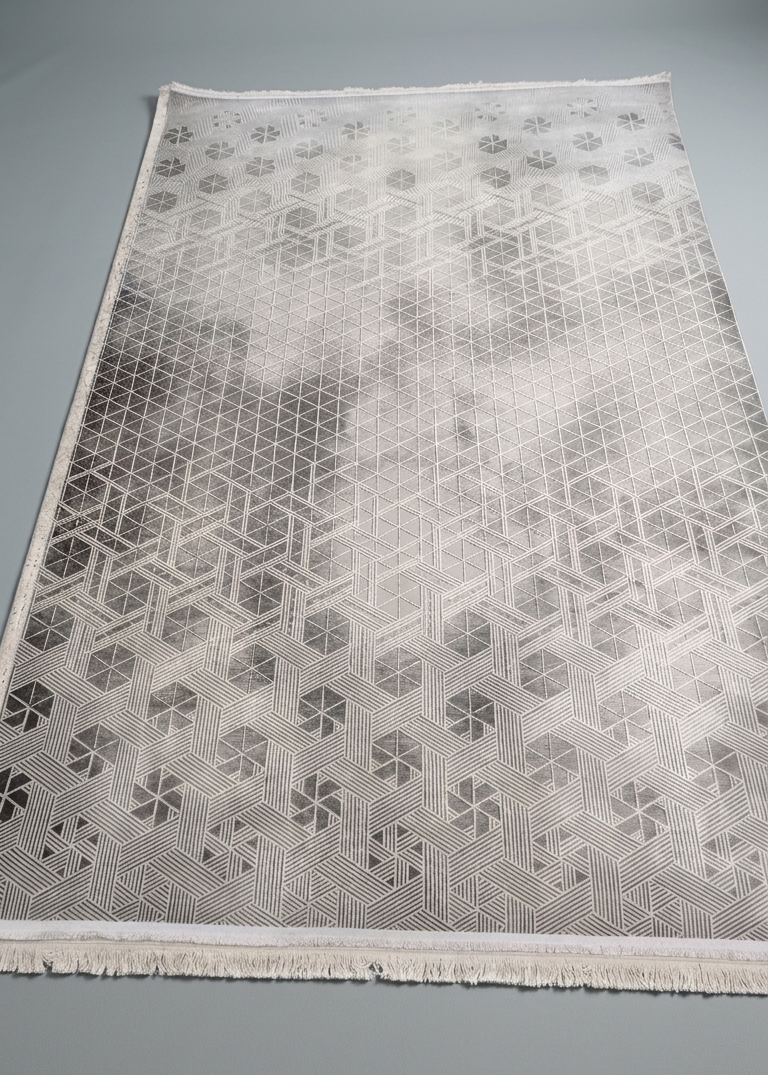 A rectangular area rug with a geometric pattern, shown flat on a neutral gray background. The rug features a gradient design that transitions from a light cream-white at the top to a darker gray at the bottom, with a fringed edge.