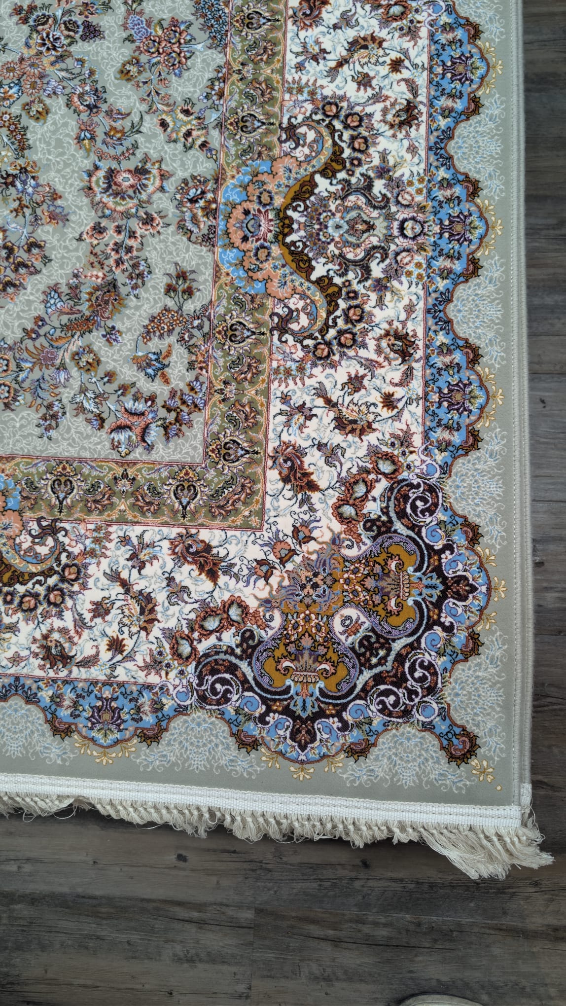 A close-up of an ornate area rug with a traditional floral pattern, featuring cream, blue, brown, and gold tones, laid out on a dark wood floor.