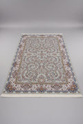 A large traditional Persian-style area rug with an intricate floral pattern, laid out on a wooden floor. The rug features a cream and beige base with blue, brown, and gold accents in its detailed motifs and border.