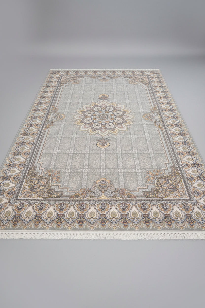 A rectangular area rug with a traditional Persian-style floral pattern, laid out on a wooden floor in what appears to be a showroom or warehouse. The rug features a light beige and gray base with cream, gold, and muted blue accents in its intricate medallion and border designs.