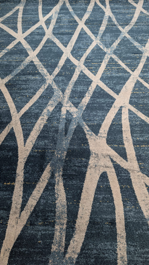 A close-up of a textured area rug featuring an abstract, organic wavy pattern in cream and slate blue.
