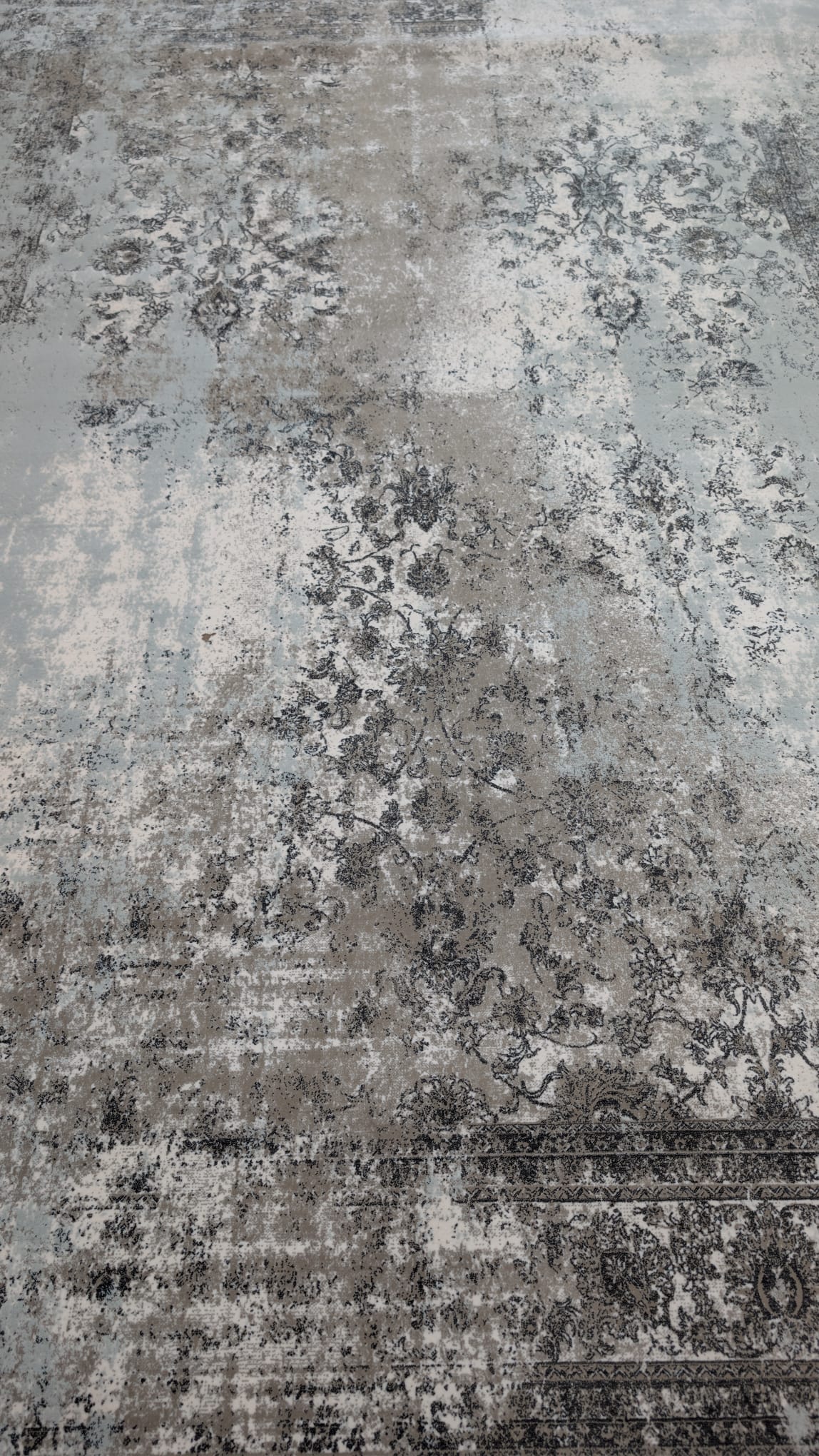 A distressed vintage-style area rug with an abstract, faded floral pattern in shades of gray, beige, and off-white.