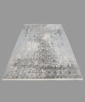 A large rectangular area rug with a distressed traditional pattern in shades of gray, beige, and off-white, laid out on a wooden floor. A person's feet in white sneakers are visible at the bottom edge of the frame.